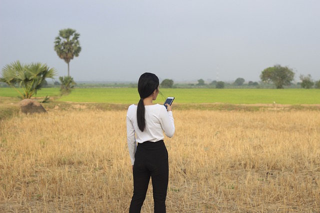 a woman in a field holding a phone, pictured from back
